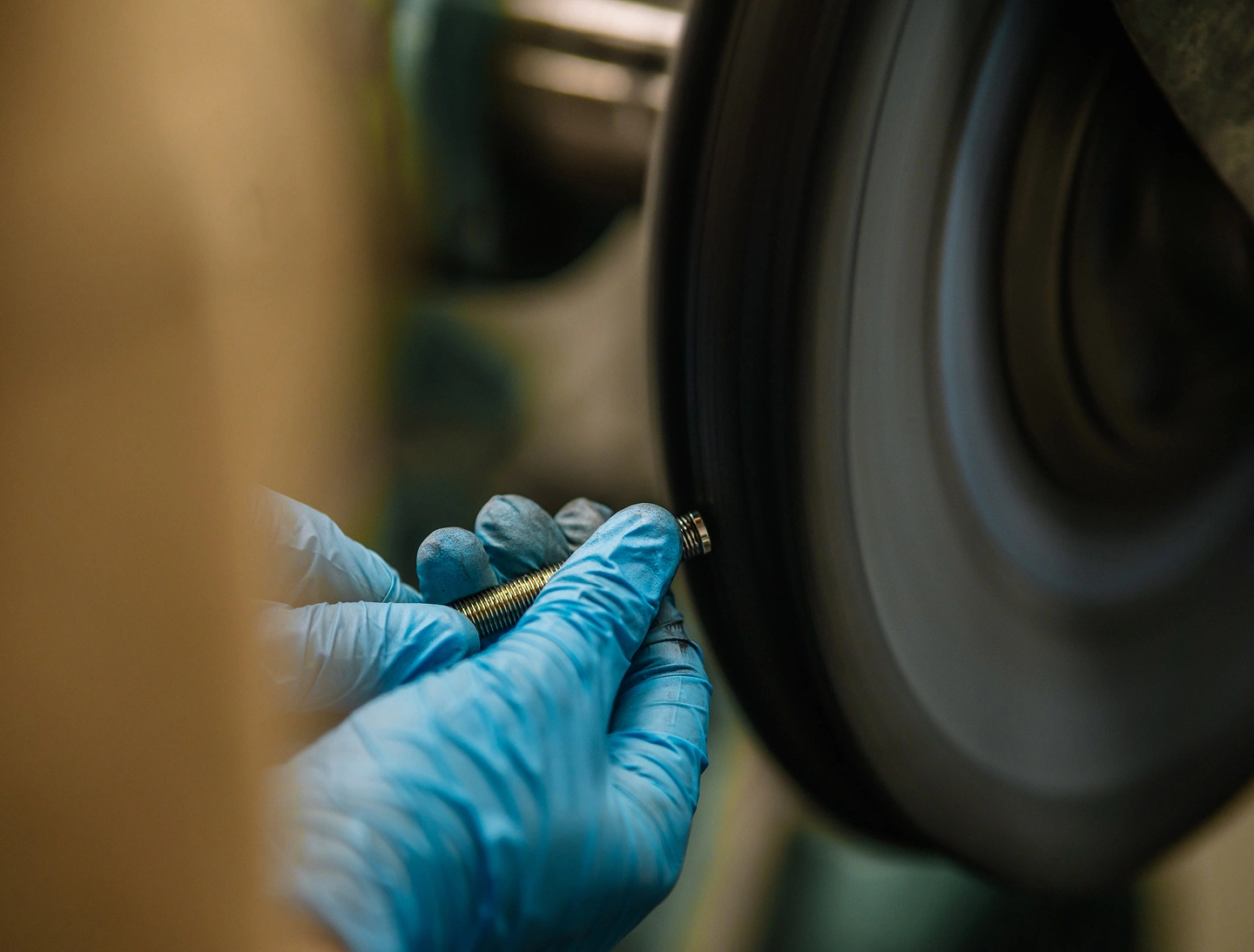 Een APAK-medewerker polijst een metalen onderdeel met blauwe werkhandschoenen aan een polijstmachine.